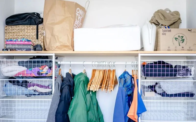 A minimalist open wardrobe featuring modern clothing, hangers, and storage baskets.