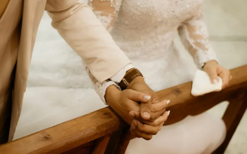Close-up of a bride and groom holding hands during their wedding ceremony, wearing elegant attire.