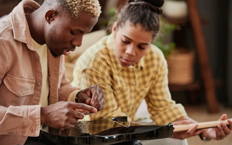 Father teaching daughter to fix guitar strings at home, bonding over music.