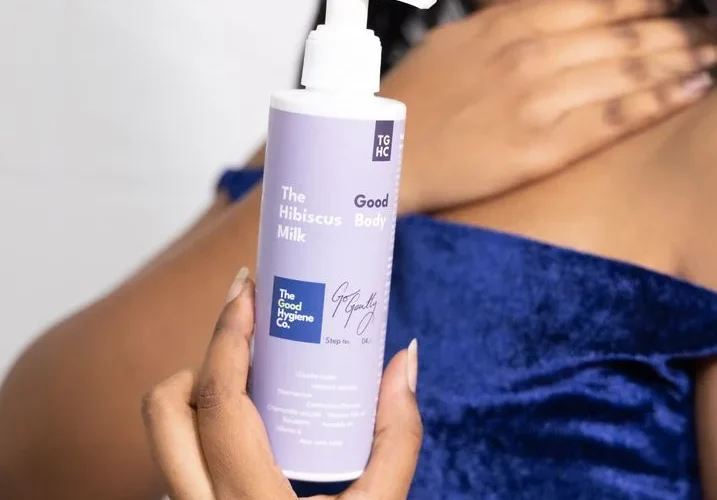 A close-up of The Hibiscus Milk skincare lotion being held by a woman, emphasizing soft skin care.