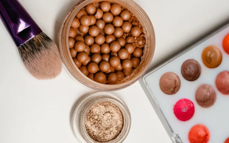 A flat lay showcasing makeup brushes, bronzer pearls, and a lip palette for beauty and cosmetic use.