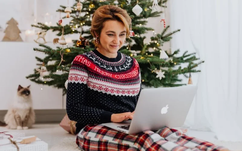 Woman enjoying wireless technology at home with cat during festive Christmas season.