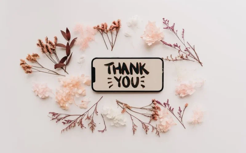 Flat lay of dried flowers surrounding a smartphone displaying a thank you message.
