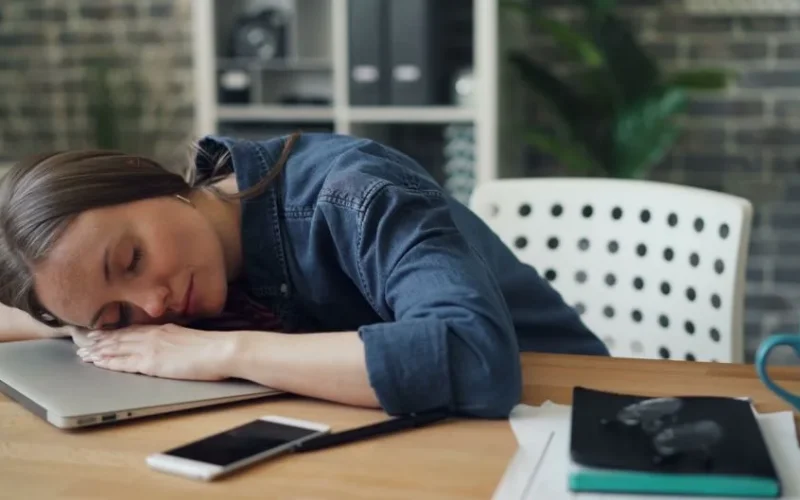 Tired woman resting her head on a laptop at an office desk, symbolizing workplace fatigue.