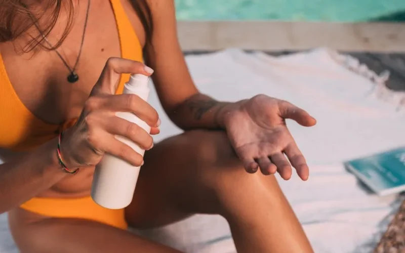 Close-up of a woman using sunscreen spray on a sunny day by the pool.