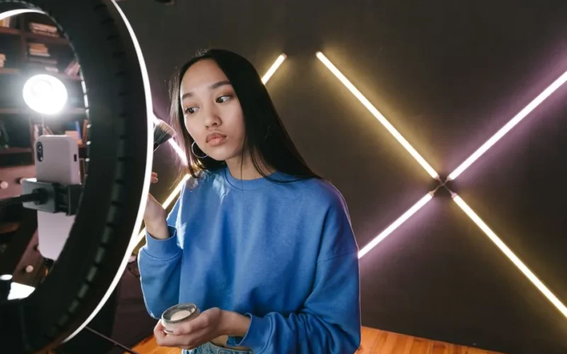 Woman applying makeup under ring light in modern indoor setting, perfect for beauty content creators.