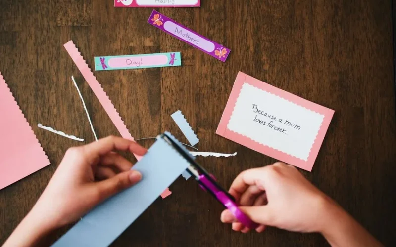 A child creating a personalized Mother's Day card with colorful paper and scissors.