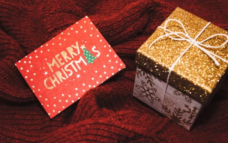 A joyful scene with a 'Merry Christmas' card and a glittery gift box on red fabric.