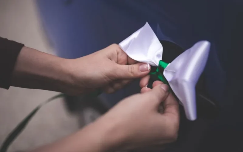 Close-up of hands tying a white ribbon on a car door handle, emphasizing detail and elegance.