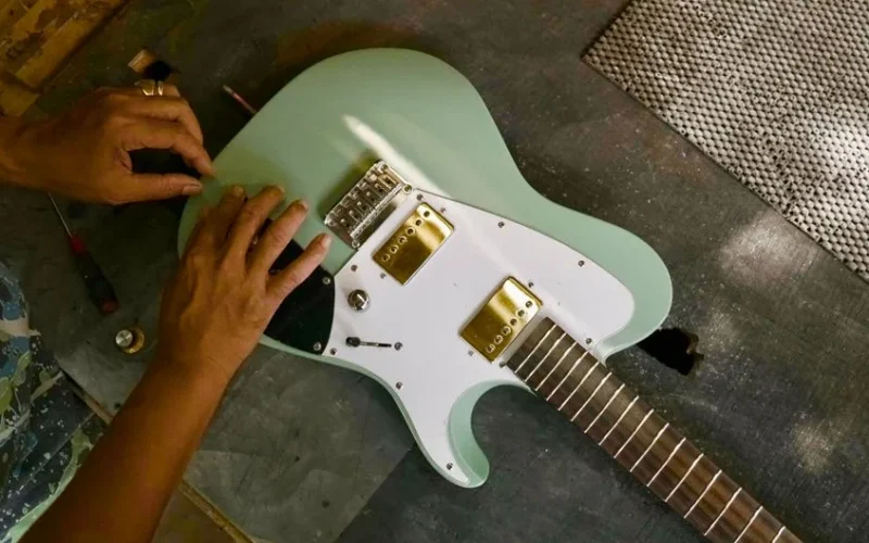 An artisan carefully assembling a mint green electric guitar in a workshop setting.