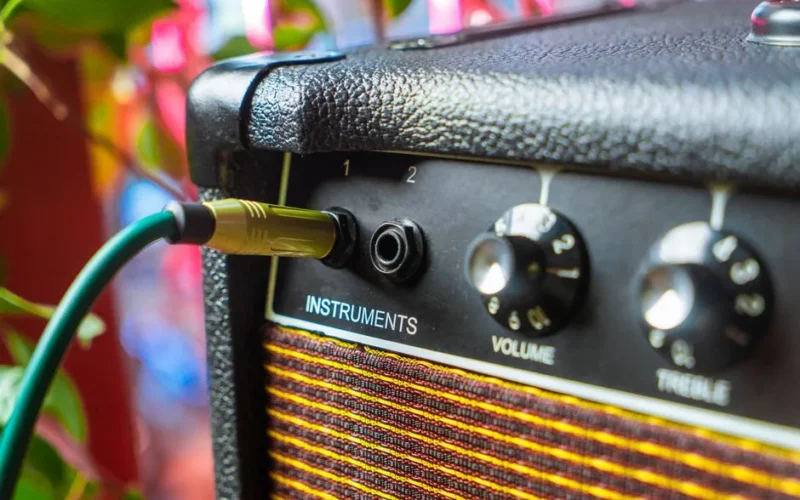 Detailed close-up of an amplifier with an instrument cable plugged into the input, showcasing volume and treble knobs.