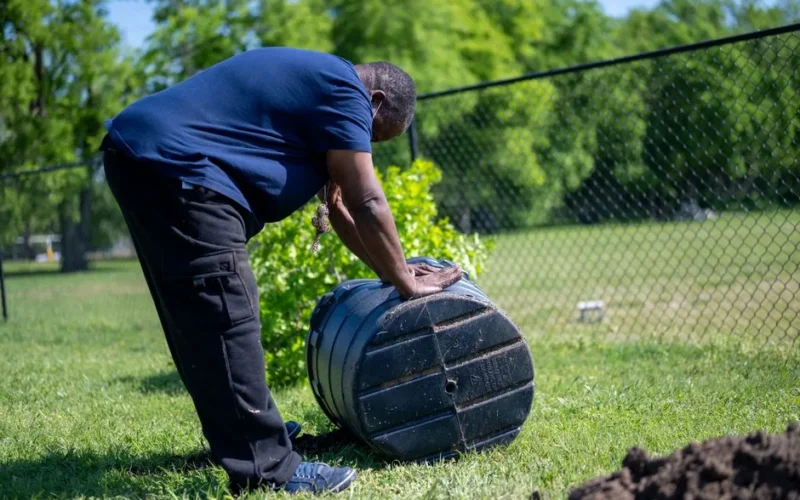 A man working with a compost bin in a sunny park, promoting outdoor gardening activities.