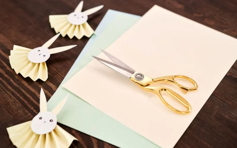 Colorful paper cutouts of rabbits with a pair of gold scissors on a wooden table.