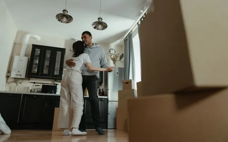 Happy couple dancing together in their new home filled with moving boxes, celebrating new beginnings.