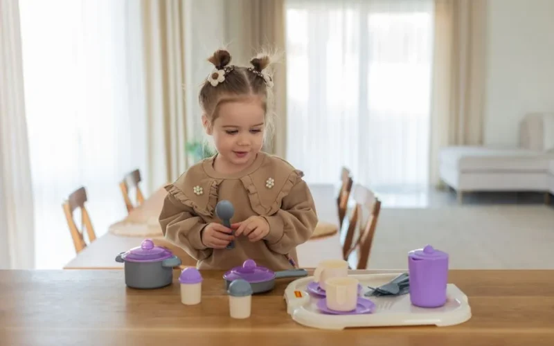 Little girl enjoying imaginative play with toy kitchen set in a cozy, well-lit room.