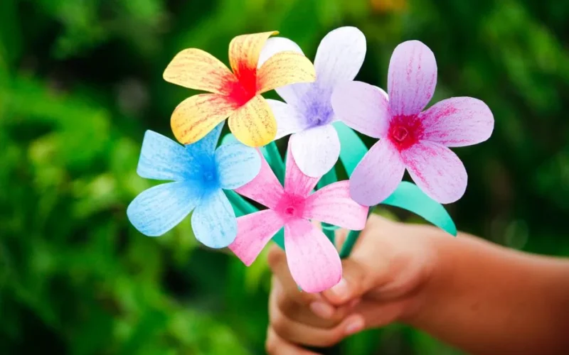 Colorful handmade paper flowers held in a hand against a lush green background, showcasing creativity and DIY art.