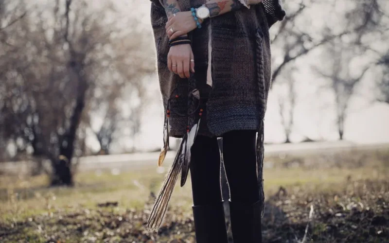 Person holding a dreamcatcher outdoors with a bohemian style in a park.