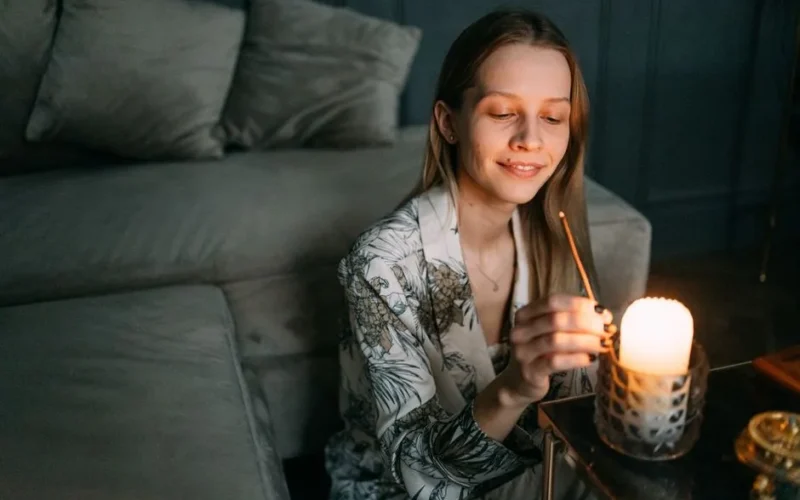 A woman sitting indoors, lighting a candle for a calming meditation session, creating a warm, serene ambiance.