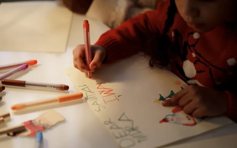 A young girl writes a letter to Santa using colorful markers during the Christmas season.