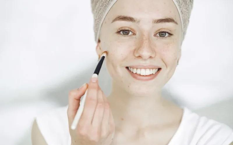 Close-up of a smiling woman applying makeup with a brush, enhancing natural beauty.