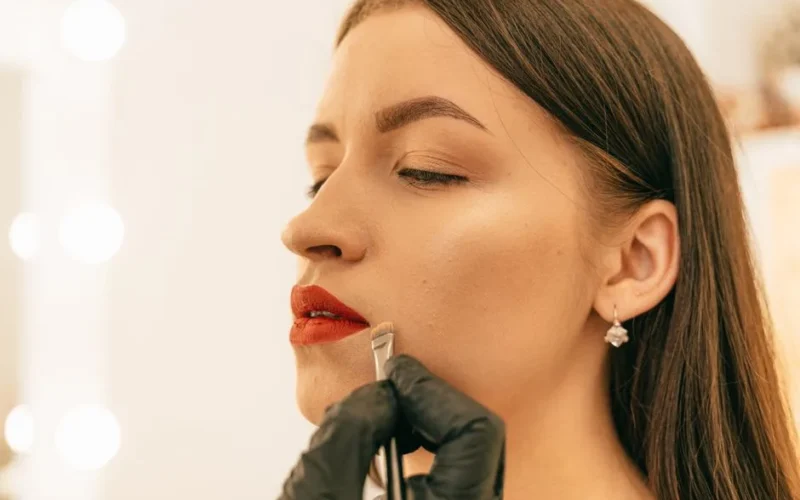 A close-up shot of a woman having her lipstick applied by a makeup artist.