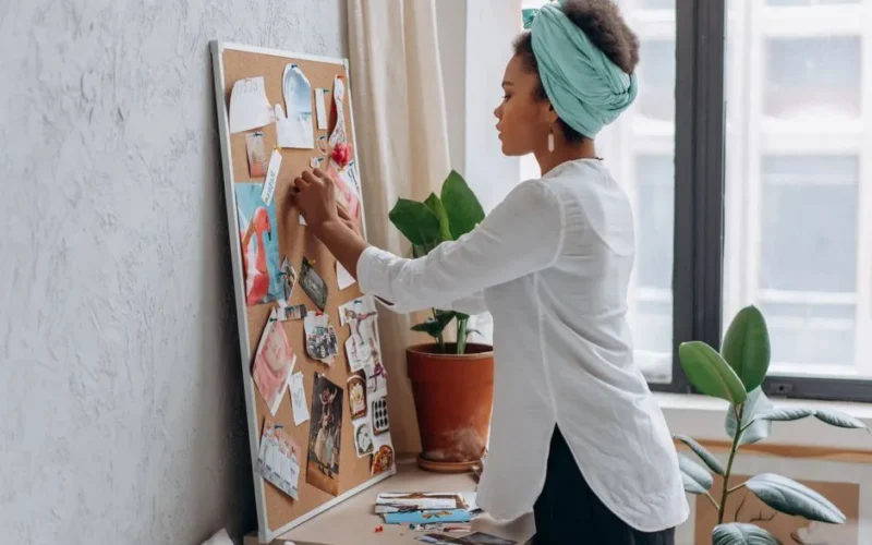 Woman in white shirt arranging a vision board in a modern apartment.