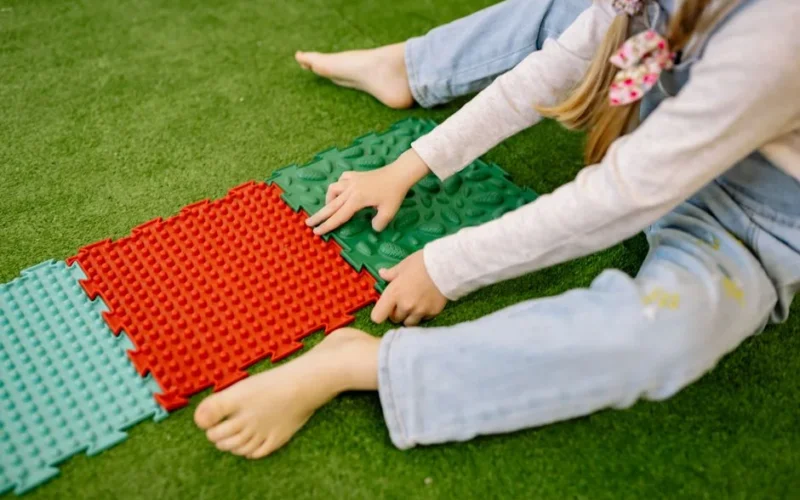 A child plays with colorful textured mats on grass, enjoying outdoor recreation.