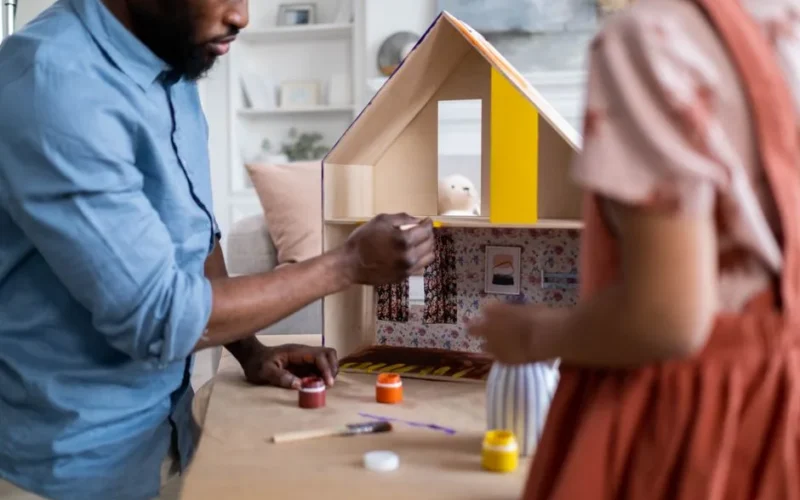 A man and a child painting a dollhouse together, focusing on creativity and craftsmanship.