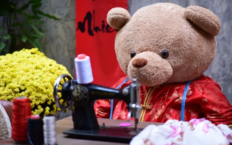 Cute teddy bear sewing with a vintage machine, surrounded by colorful threads and flowers.