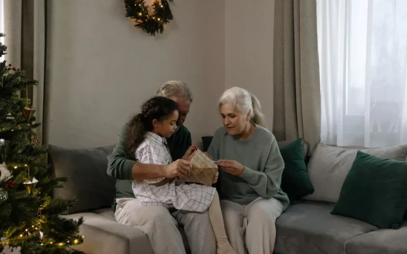 A happy family moment with grandparents and granddaughter opening a Christmas gift together.