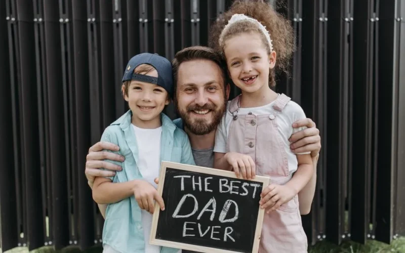 A joyful father hugging his children with a "Best Dad Ever" sign.