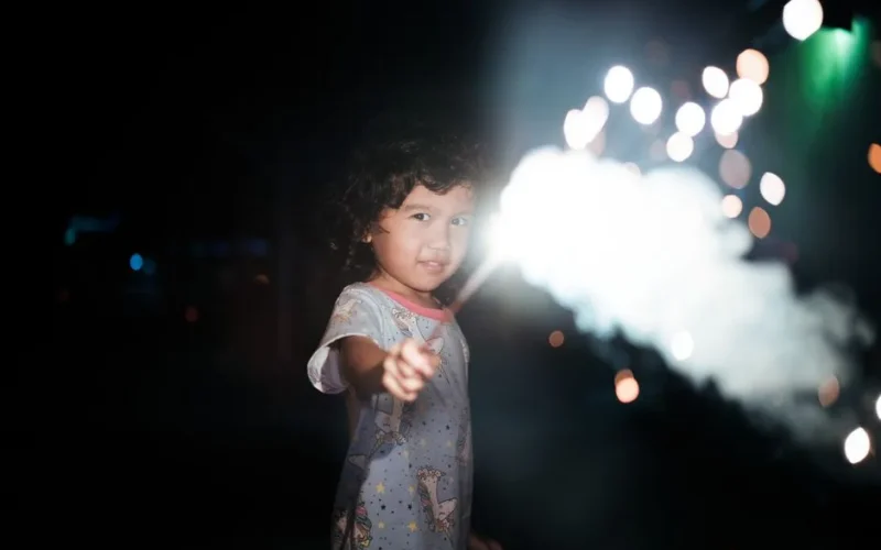 A young girl with a sparkler in hand lights up the night with joy and wonder.