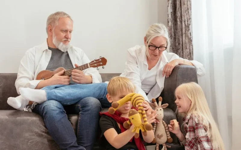 Grandparents enjoying time with grandchildren indoors, playing with ukulele and toys.