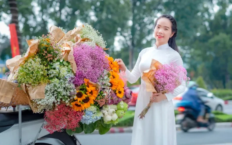 A woman in a white dress happily holding a bouquet of vibrant flowers outdoors.