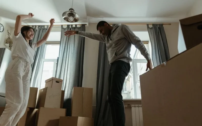 A happy couple dances among boxes in their new apartment, celebrating their move-in day.