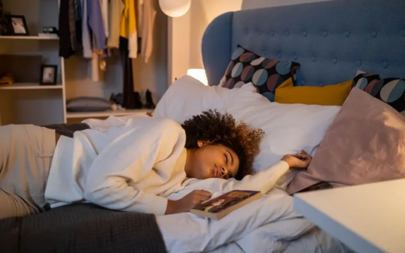 A young girl peacefully asleep on a bed holding a book, surrounded by cozy decor.