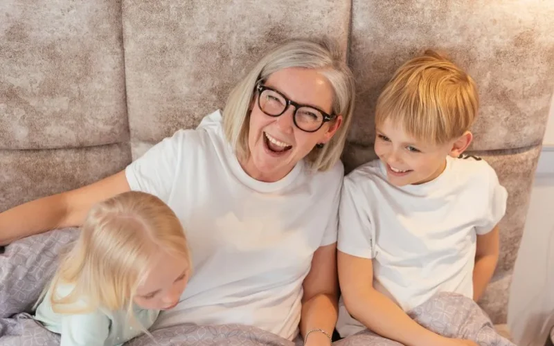 A joyful grandmother with her grandchildren in bed, sharing a happy moment indoors.