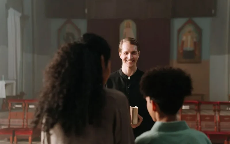 A priest smiling warmly at a family inside a church, conveying a welcoming atmosphere.