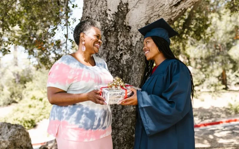 Mother and daughter sharing a joyful graduation moment outdoors with a gift.