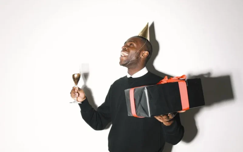 Happy man celebrating with party hat, gift, and champagne. Festive and joyful mood.