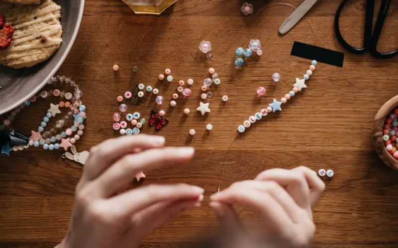 Hands crafting personalized jewelry with beads at a well-organized wooden table.