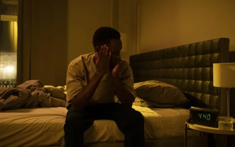 African American man sitting on a bed struggling with insomnia at night.