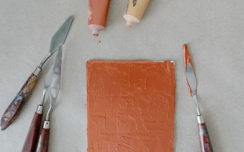 Close-up of a textured acrylic knife painting with art tools on canvas.