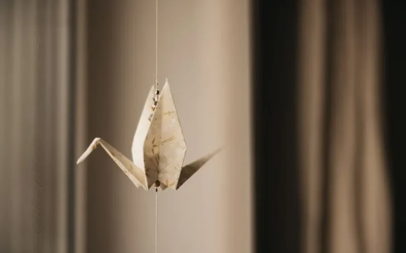 Minimalist close-up of a crafted origami crane suspended indoors.