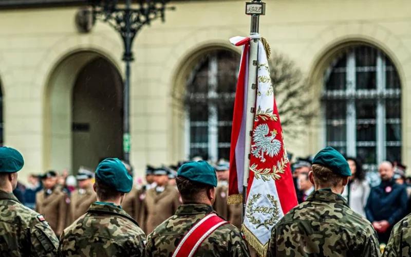 Polish soldiers in uniform during a ceremonial parade with national flag.