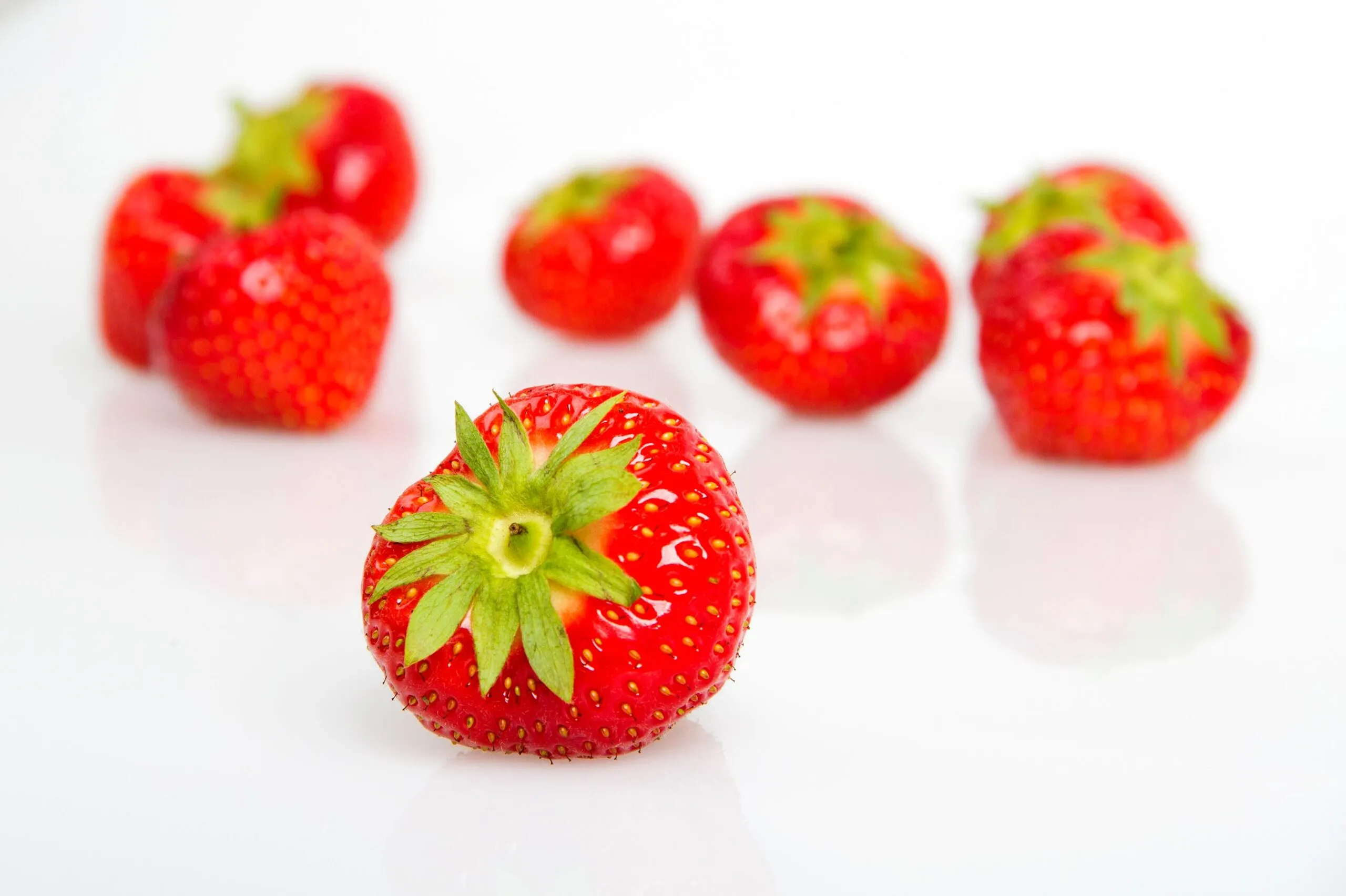 Close-up of juicy, fresh strawberries with green tops on a clean white surface.