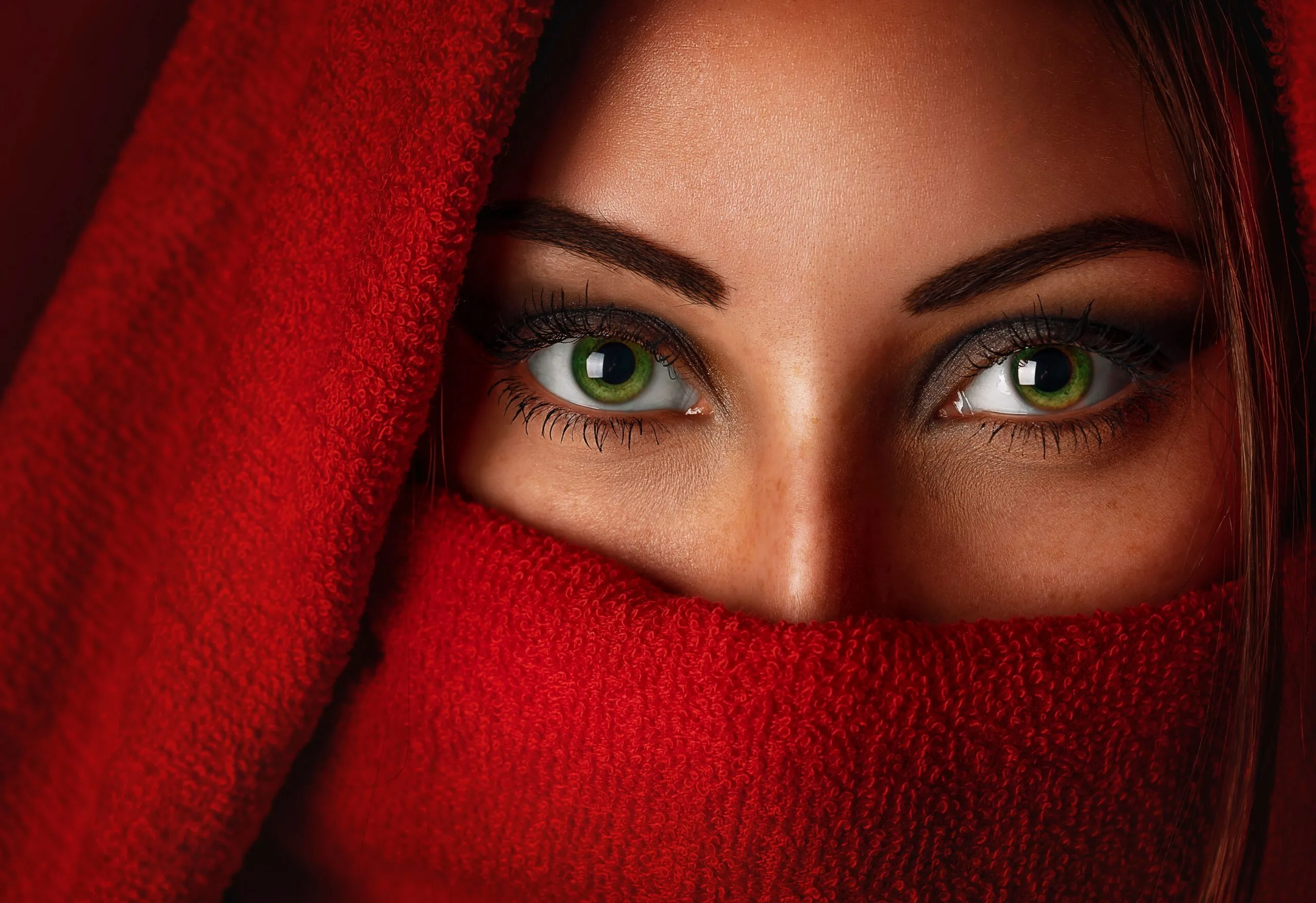 Captivating portrait of a woman with striking green eyes wrapped in a red scarf.