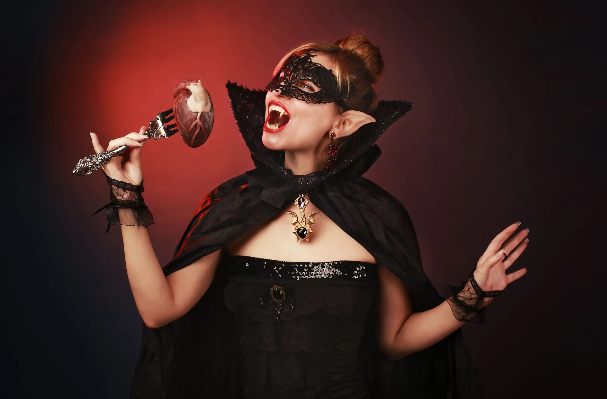Mysterious woman dressed as a vampire with a gothic mask and cape, holding a fork