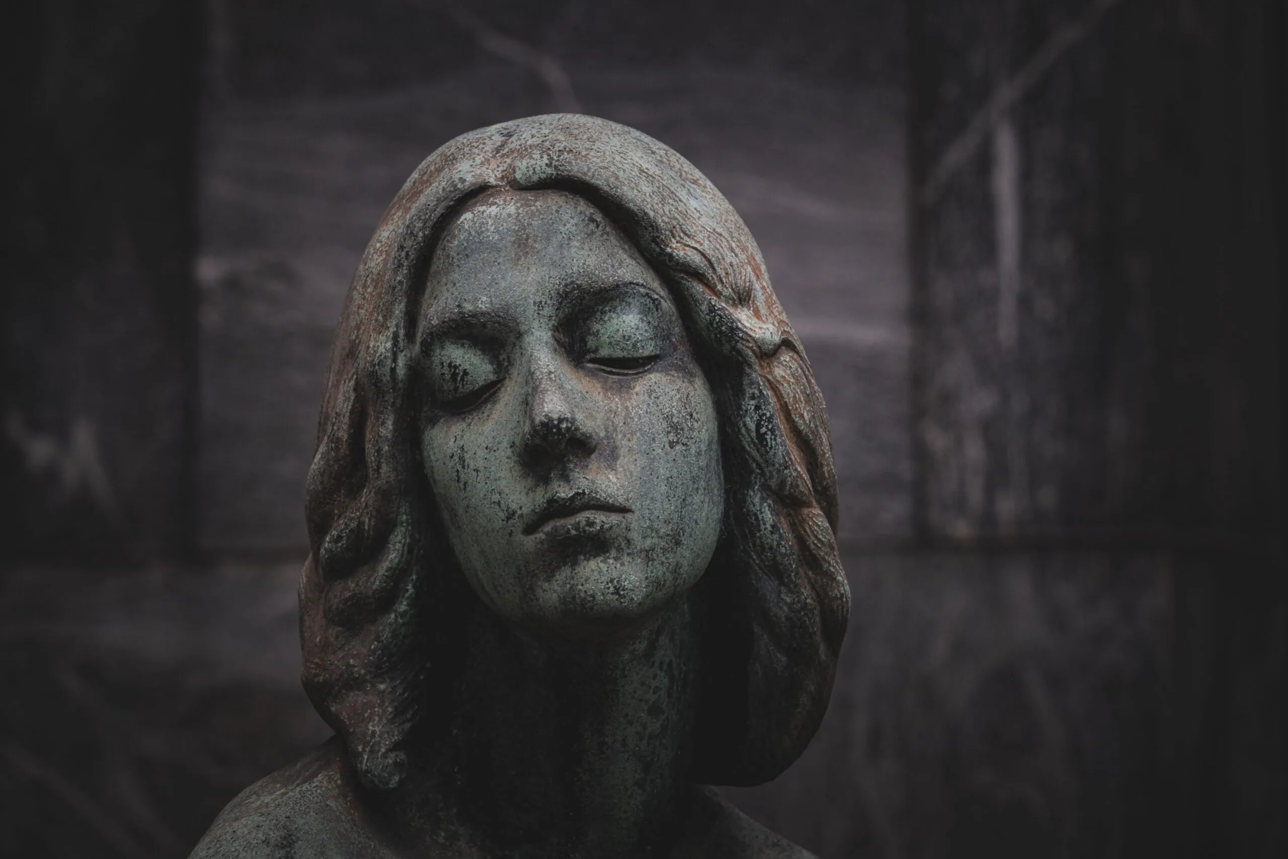 Close-up of a serene stone statue with a green patina finish, set against a dark background.