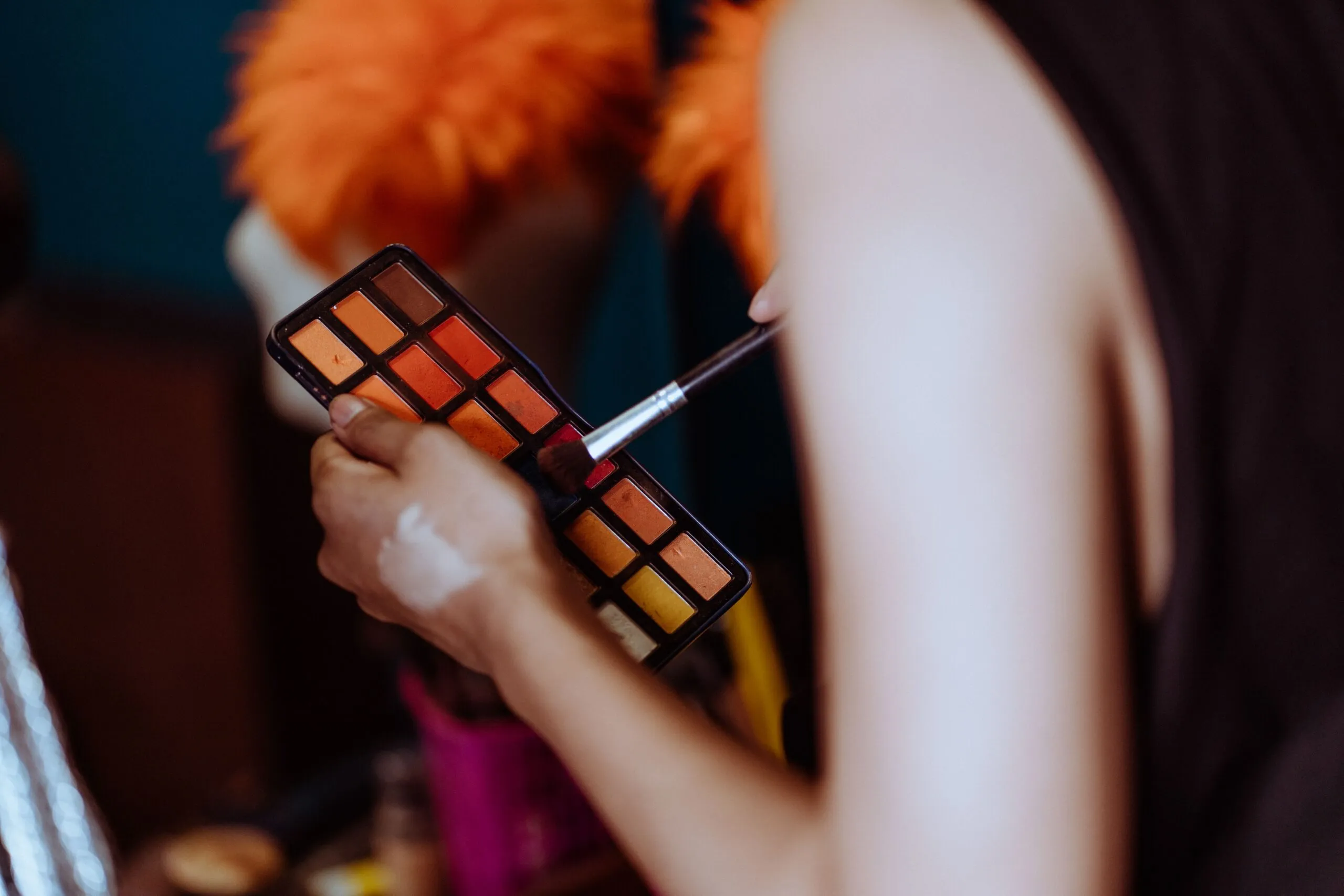 Crop ethnic anonymous visagiste putting eyeshadow with brush while creating makeup in studio